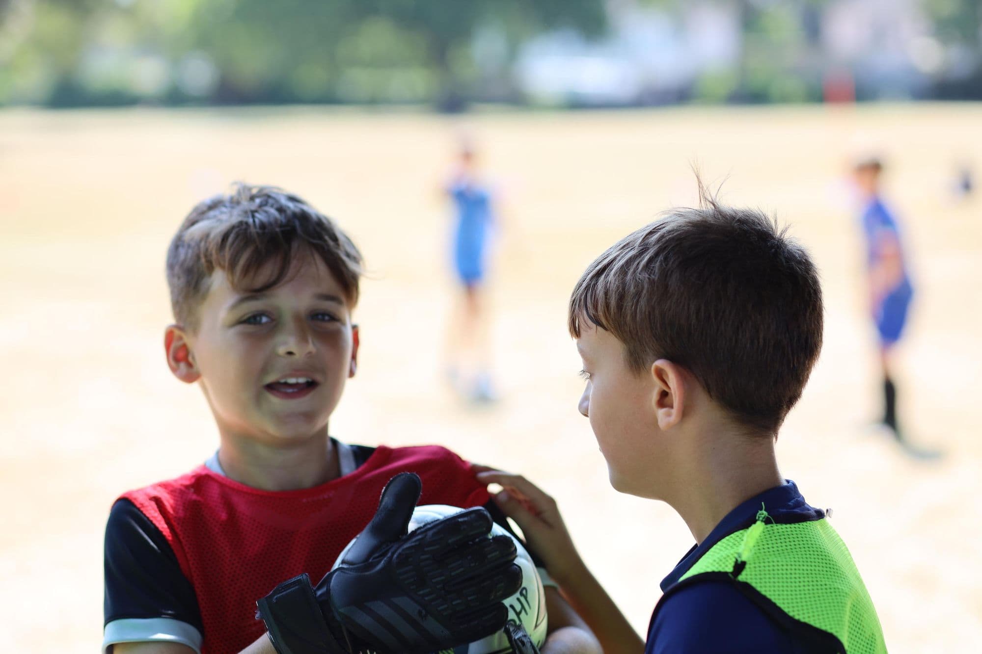 Two young players smile at each other, one holding goalkeeper gloves